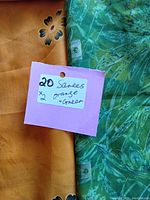 Photo showing orange saree fabric with beige floral and geometric patterns and adjacent green-blue fabric with foliage design along with a pink tag indicating 20 sarees, 2 each of orange and green.