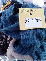 Close-up photo showing a blue vertically striped top with a handwritten tag stating '30 3 Tops' and markings 'V 805 / 905'.