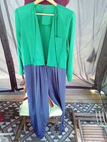 Full view of green and blue dress jumpsuit hanging on hanger showing top and bottom halves