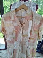 Beige short sleeve dress with patchwork pastel pattern hanging on a hanger