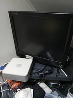Photo showing Apple Mac Mini computer unit alongside black LCD monitor and some cables.