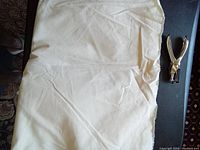Full view of off-white muslin fabric piece, folded and laid on a flat surface with some creases visible, alongside a metal hole punch for scale.