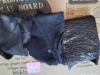 Three black fabric remnants laid out, showing different textures including plain satin-like, velvet-like, and patterned fabric.
