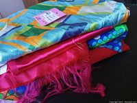 Photo showing several folded fabric pieces with vibrant geometric and floral mod patterns and solid linings, along with a pink tag indicating yardage and lot ID.