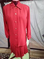 Red long-sleeve button-up blouse and pleated skirt set by Mister Leonard, displayed on a dress form.