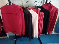 Six women's vintage blouses and tops hanging on hangers, displaying colors and some design details, including red, black pinstriped, and cream shades.