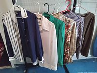 Seven vintage women's blouses and tops hanging on hangers, showing variety of colors and patterns fitting sizes 8 to 14.