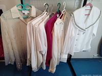 Six vintage women's blouses and tops hanging on hangers, showing overall styles and colors.