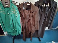 Three vintage women's suits on hangers including green bejeweled jacket, brown faux suede jacket and skirt, black pinstriped knit jacket and pants.