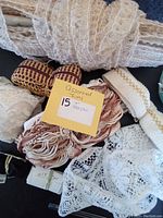 Close-up photo showing multiple vintage trims including lace, elastic, and woven fabrics in neutral and maroon tones.