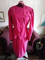 Front view of pink silk jacket and skirt set displayed on dress form showing asymmetrical button closure and fabric pattern.