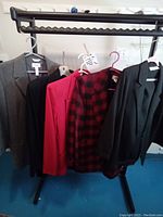 Four vintage women's jackets on hangers on a rack. Gray, red, red and black checkered, and dark green or black colored jackets visible.