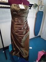 Front view of the sable brown satin strapless formal gown on a dress form, showing ruched bodice, built-in brooch under bust, and smooth satin skirt.