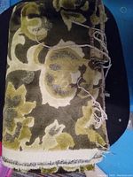 Folded vintage green upholstery fabric with floral flocked pattern, showing texture and color variation.