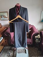 Full view of dark gray women's Kasper pantsuit displayed on dress form with pants hung on hanger in front.