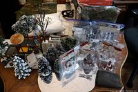 Wide view of the entire lot on table including trees, figurines, moon light, bags of snow, street lamps, fencing, skating rink and paving pieces.