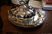 Silver-plated trays and covered bowl with lid arranged on a table, showing polished reflective surfaces and decorative edges.