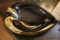 Top angled view of the black and gold ceramic centre piece showing its sweeping organic shape with gold overlay detail.