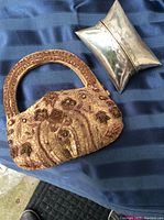 Photo showing both vintage bags: the beaded gold handbag and the silver plated clutch on a blue striped fabric background.