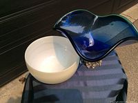 Photo showing white opalescent glass bowl-shaped vase and cobalt blue swirling glass vase with metal base side-by-side on blue fabric