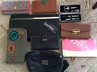 Overview of 8 clutches and a nail grooming kit arranged on carpeted floor showing different colors, materials, and styles for a ladies collection.