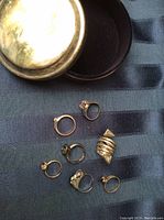 Seven vintage silver rings arranged outside the silver-plated box to show individual ring designs and the box lid beside it