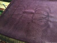 Close-up photo of deep purple wool area rug showing thick pile and visible furniture markings on surface.