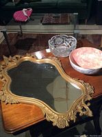 Photo showing all three items together on a wood table: the ornate faux Victorian mirror with gold frame, clear cut crystal bowl, and mottled pink ceramic bowl.