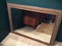Full view of the large rectangular mirror showing the patterned gold frame and reflective glass surface leaning against a wall.