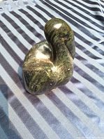 View of large soapstone pelican sculpture showing polished, rounded form with natural stone patterns on striped fabric background.