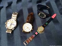 Photo of four men's wristwatches placed on a dark striped fabric background. Watches are Diesel with silver metal band, Fossil with brown leather band (band needs new pin), Polar black digital watch, and colorful Swatch watch.