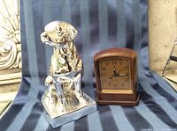 Photo showing mercury glass dog figurine and bronze patina desk clock side by side on fabric surface.