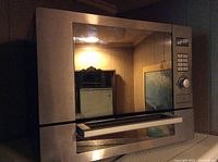 Front view of stainless steel microwave with control panel and door open showing interior light and separate grilling oven below.