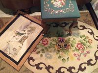 Photo showing the three antique textile items together: rectangular winter scene hooked rug, oval rose hooked rug, and green floral petit point foot stool.