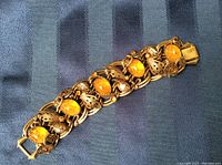 Front view of vintage bracelet showing amber stones, gold filigree, and pearls on dark fabric.