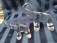 Photo of two clear crystal elephant figurines by Kosta Boda, one larger and one smaller, on a striped fabric background.