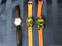 Three wristwatches displayed: Mickey Mouse watch with black strap, two orange Ninja Turtles watchbands with raised turtle figures