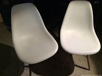 Two white dining chairs with molded plastic seats and solid beech wood Eiffel-style legs shown from front.