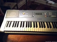 Top view of Yamaha YPT-300 keyboard showing 61 keys, control buttons, LCD display, and right speaker with discoloration on white keys.