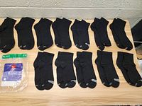 12 pairs of black Hanes ankle socks laid out on a table with one of the original empty packaging bags included showing '6 ankle' and size 5-9