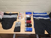 Top view of 13 pairs of men's size XL underwear laid out on a table in various colors including black, gray, blue, and red. Some pairs are packaged new.