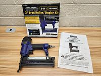 Photo showing the 18 gauge 2 inch brad nailer and stapler tool, original box with product image and text, and the instruction manual laid out against a wall.