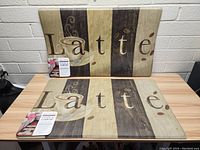 Two vertically striped kitchen mats with "Latte" text and coffee cup image, shown standing against a white brick wall.