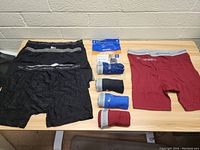 Top view of eight pairs of men's boxer briefs in various colors on a table against a wall, some folded and others rolled, with Gildan packaging visible.