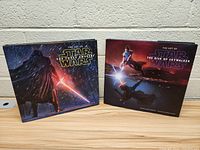 Two hardcover Star Wars art books titled 'The Art of Star Wars: The Force Awakens' and 'The Art of Star Wars: The Rise of Skywalker' are placed upright on a wooden table against a beige wall.