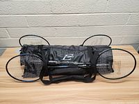 Four badminton rackets positioned on and around a black Acepoint branded sports bag on a light wooden surface against a white brick background.