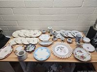 Overview of vintage plates and serving dishes arranged on a table showing variety of floral and decorative patterns and styles.