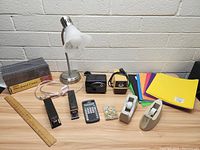 Photo showing full lot contents on desk including lamp, sharpeners, staplers, ruler, calculator, tape dispensers, push pins, jewel cases, and colored paper.