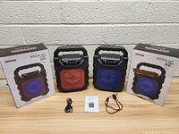 Two Boom-M2 Bluetooth speakers (red and blue) with power cables, manuals, and boxes against a white brick wall.