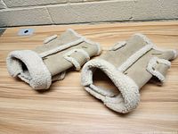 Two beige sherpa style dog coats laid flat on a wooden table showing front side, sherpa lining, and velcro strap details.